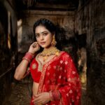 Beautiful Indian woman in a red saree with jewelry, posing in an ancient building setting.